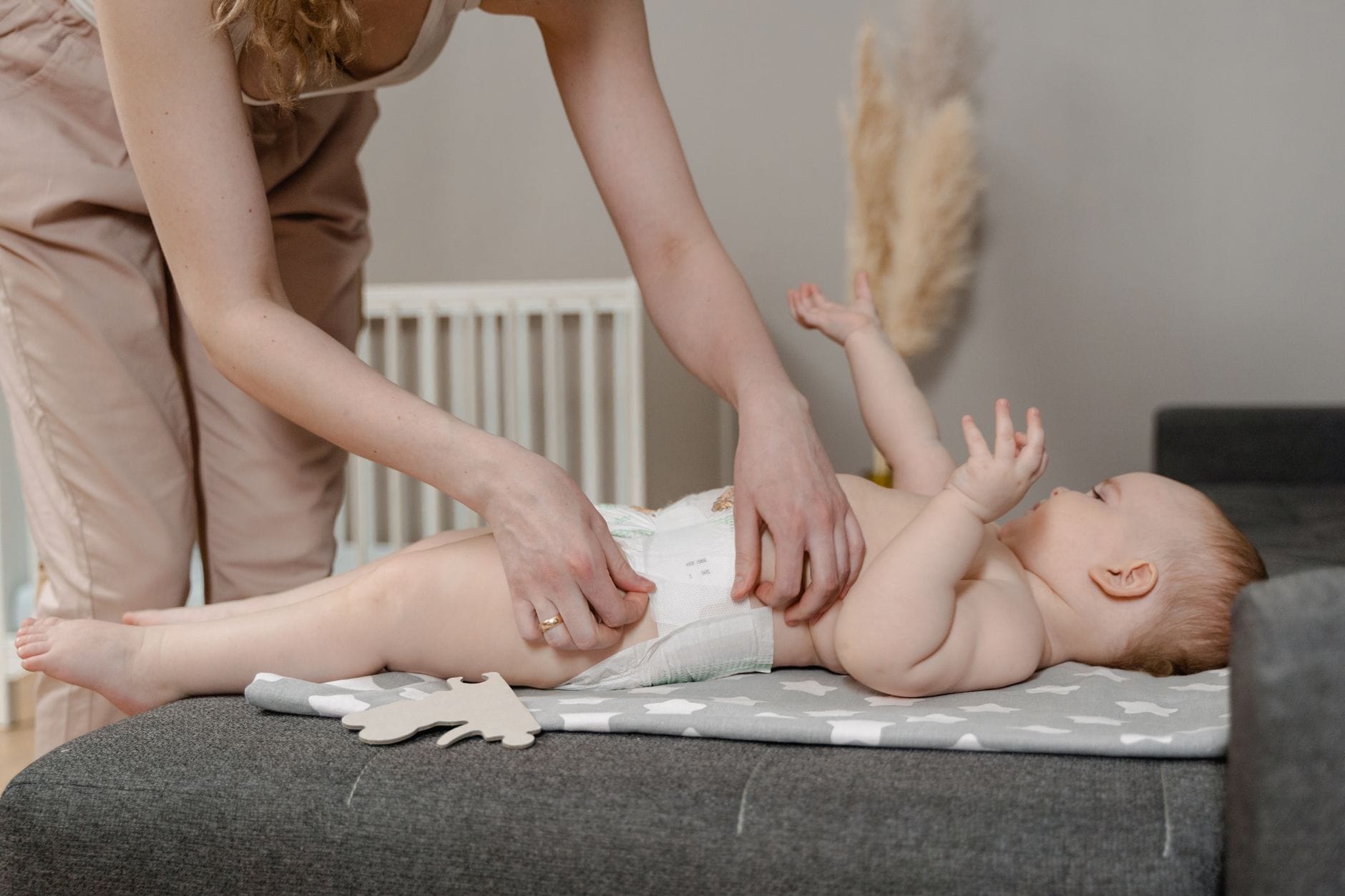 Mama zmienia niemowlęciu pieluchę na szarej macie w domu