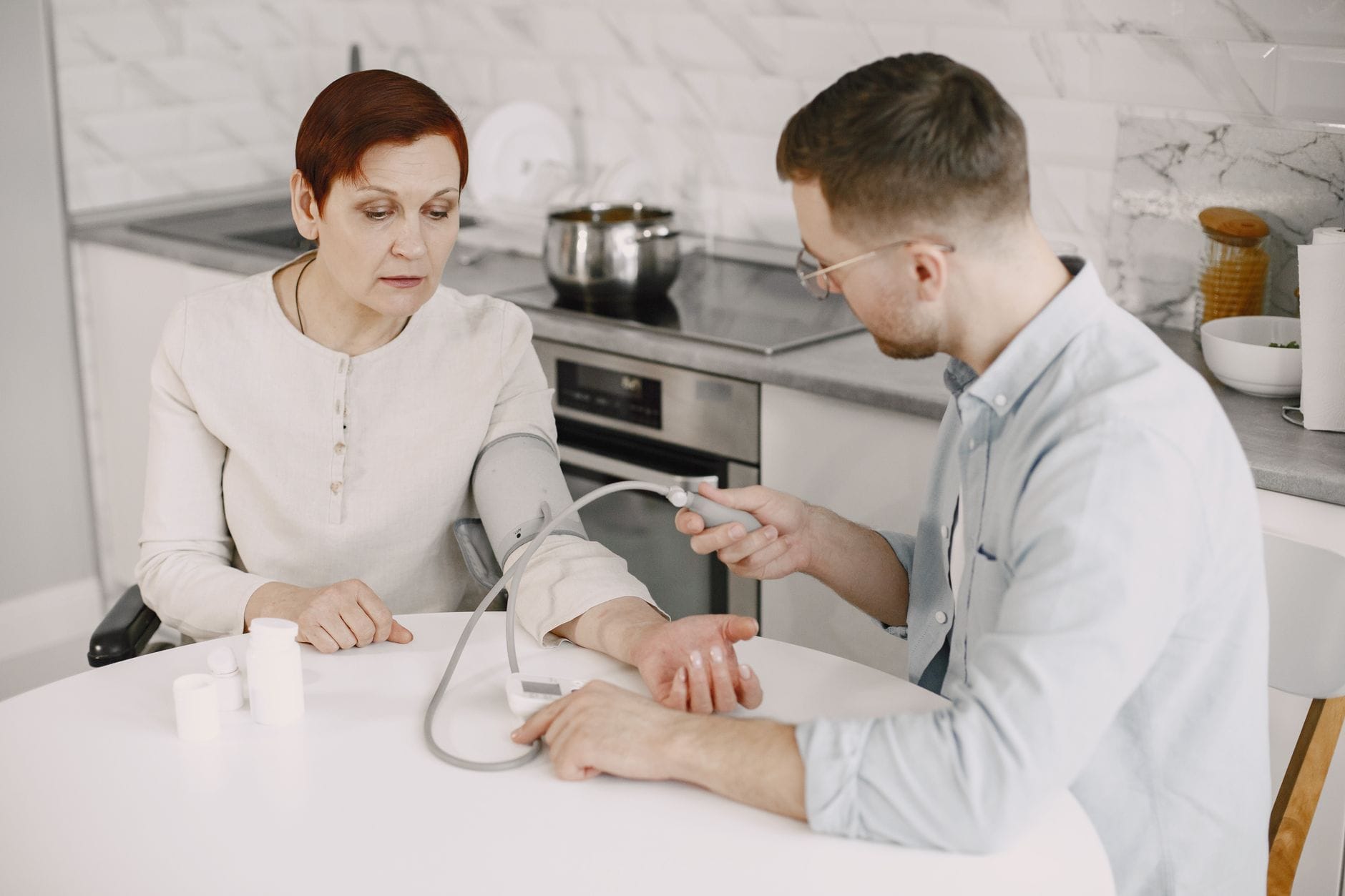 Mężczyzna mierzy ciśnienie starszej kobiecie przy kuchennym stole